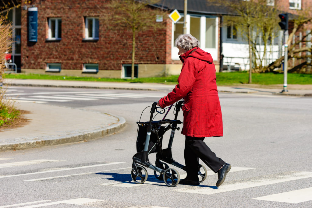 Lund, Sweden - April 11, 2016: Real life in the city. Elderly woman is out walking, crossing a street with her walker. No traffic visible.