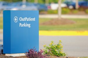 "Arrow sign for outpatient parking in front of parking lot, horizontal with copy space to right."