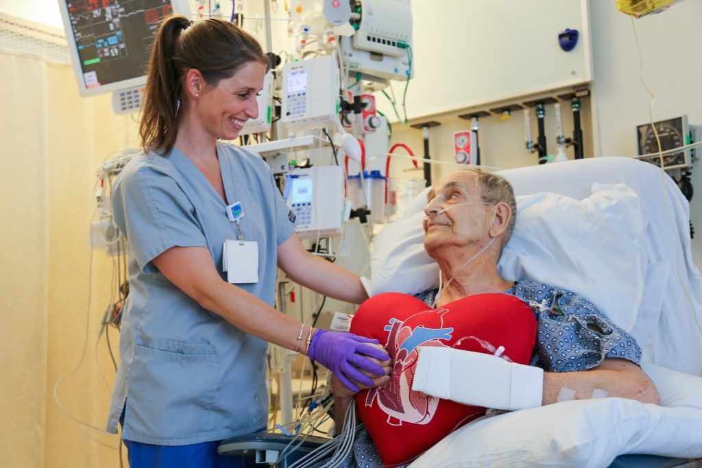 Julie Crowell, BSN, RN, helps patient James Mitchell sit up in a chair as part of the Cardiac Surgery ERAS pathway.