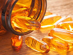 Brown bottle of vitamin D and fish oil capsules spilling onto wooden surface