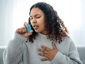 Black woman at home holding chest with one hand and about to take her inhaler with the other
