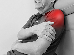 Elderly man leaning back holding left arm where pain is highlighted red coming from upper shoulder