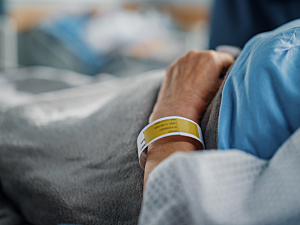 Close up of female patient lying on hospital bed with ID bracelet, recovering from surgery