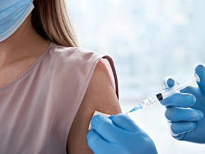 Doctor with blue gloves gives vaccine shot to shoulder of a woman