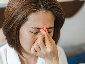 Asian woman pinches her brow, highlighted red for concept of rhinosinusitis pain