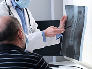 Doctor holds up x-ray of spine to show older patient