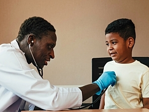 Male pediatrician listening to boy's heart through stethoscope in medical setting
