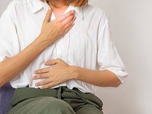 Woman sitting holding chest and stomach, red highlight on upper chest for reflux discomfort