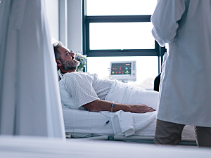 Male patient lying in hospital bed smiling up at doctor standing bedside