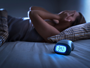 Woman in bed covering face, unable to sleep. Alarm clock on bed reads 3:41