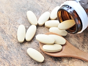 Vitamin c oval tablets spilling out of pill bottle into a wooden spoon and onto wooden surface