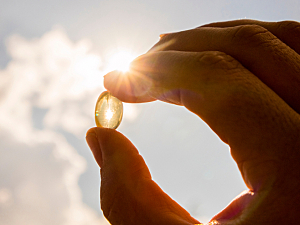 Hand holding a vitamin d supplement pill up to the sky, with bright sun
