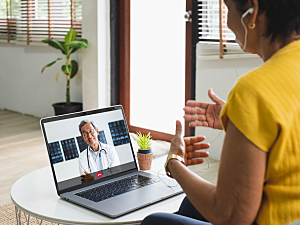 Female patient speaking to doctor via virtual telehealth appointment on laptop