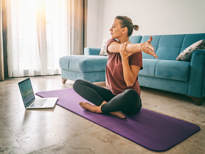 Woman stretching on yoga mat at home in front of laptop, remote exercise concept