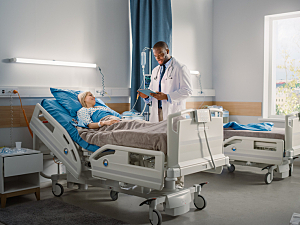 Doctor standing next to patient recovering in bed at hospital, inpatient