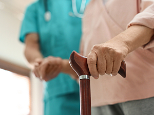 Close up of geriatric woman holding cane and being helped by medical professional