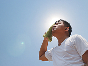 Young man standing under hot bright sun and clear sky, wiping sweat from forehead