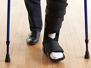 Close up of person using crutches to walk with brace on ankle and leg, broken leg concept