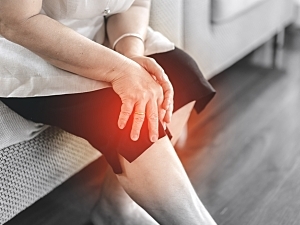 Older individual sitting on couch holding knee in pain, knee osteoarthritis concept