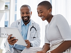 Doctor and patient look at tablet, smiling; video interpretation in medical setting