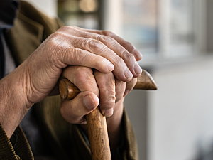 Close up of old man's hands holding wooden cane, seated