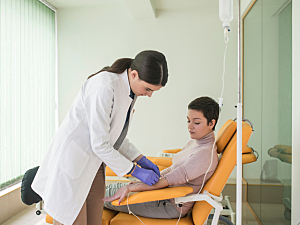 Doctor administers infusion therapy to patient sitting on chair, pegloticase infusion concept