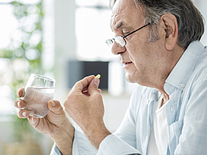 Older man holding glass of water and taking pill, paxlovid covid treatment concept