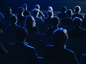 Audience Full of People in Dark Conference Hall Watching Keynote Presentation